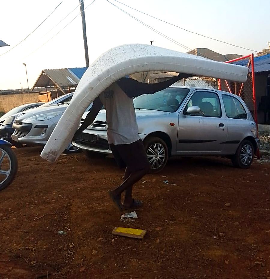 A man carries a large mattress across a lot